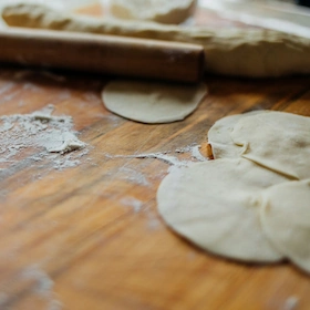 On the wooden cutting board are round dumpling wrappers and a rolling pin