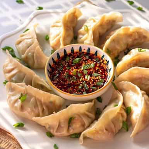 There are fried dumplings and a small plate of red Sichuan chilli oil on the white plate.